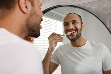 Photo of Smiling man brushing teeth near mirror in bathroom