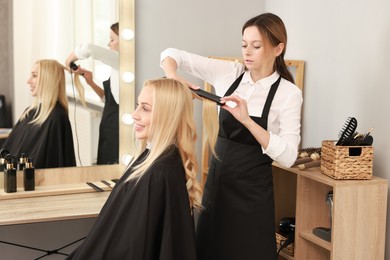 Photo of Hairdresser curling woman's hair with flat iron in salon