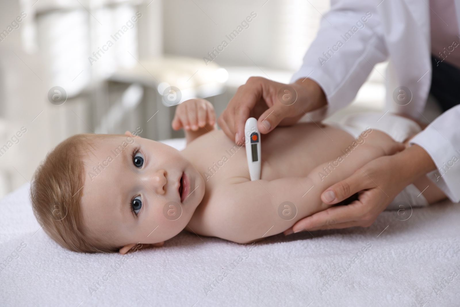 Photo of Pediatrician examining little child with thermometer in clinic, closeup. Checking baby's health