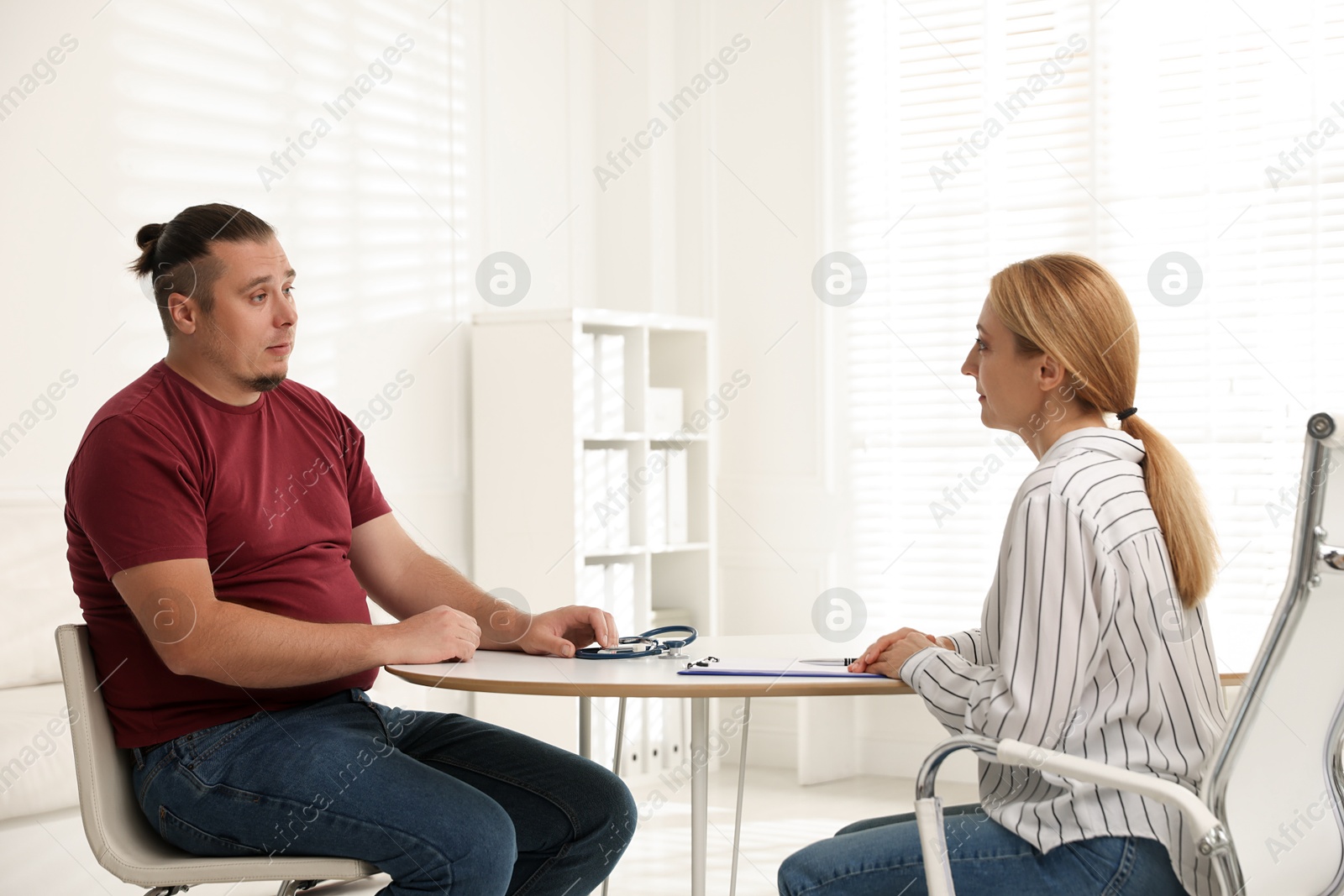 Photo of Overweight man having consultation with nutritionist at table in clinic