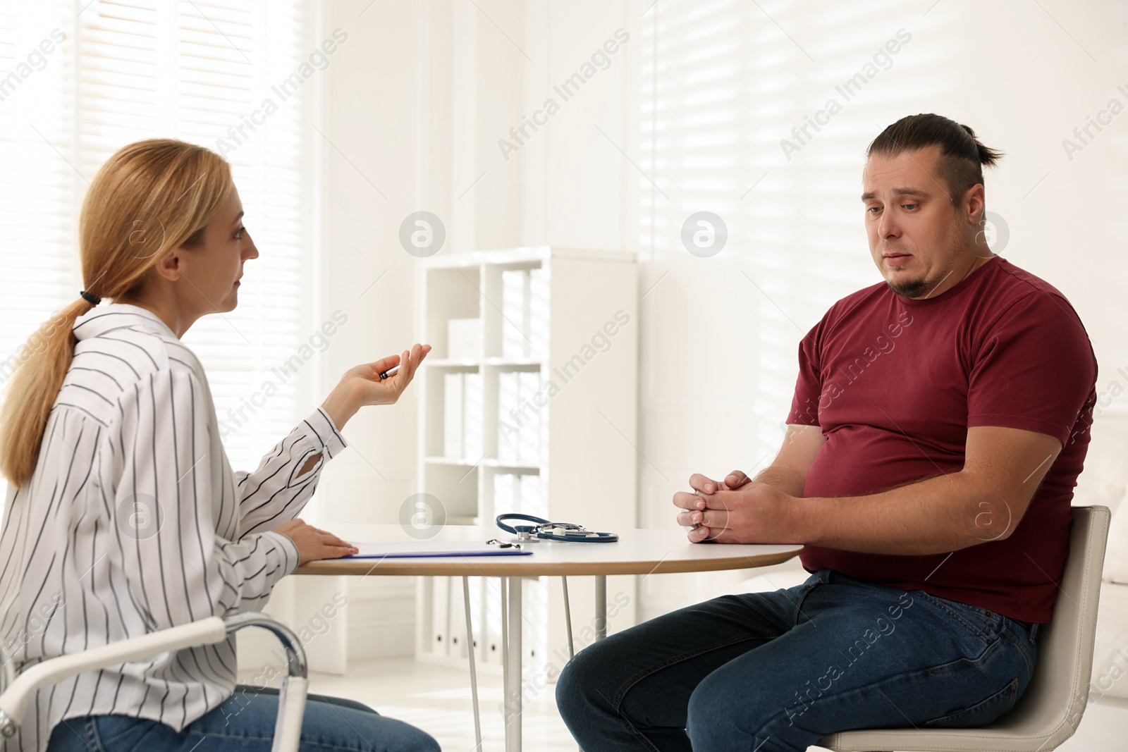 Photo of Overweight man having consultation with nutritionist at table in clinic