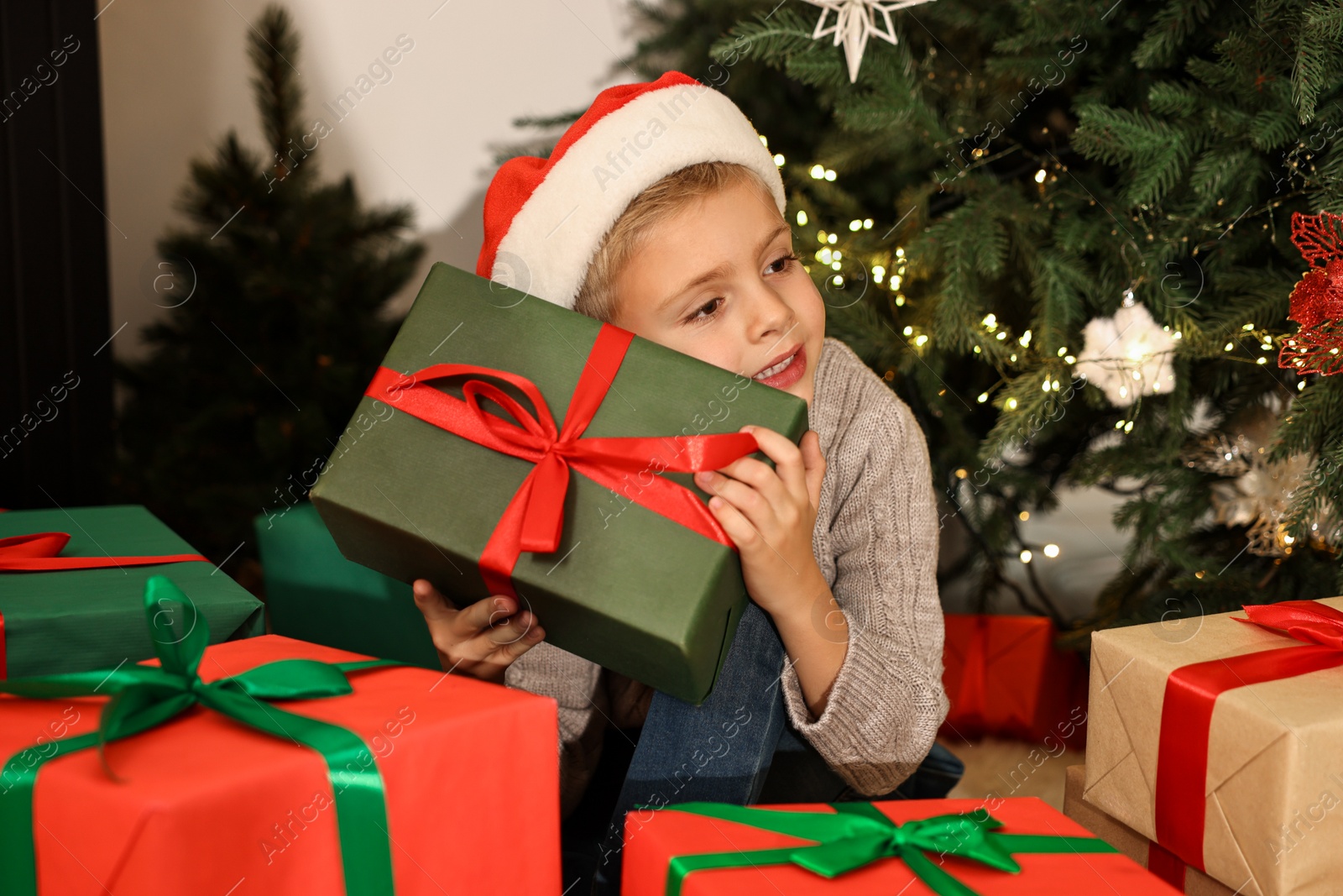 Photo of Little boy in Santa hat with Christmas gifts at home