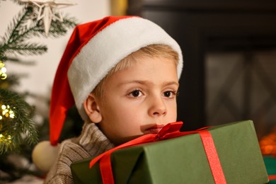 Photo of Little boy in Santa hat with Christmas gift at home