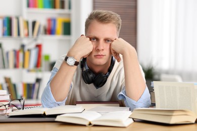 Photo of Preparing for exam. Tired student with books at table indoors