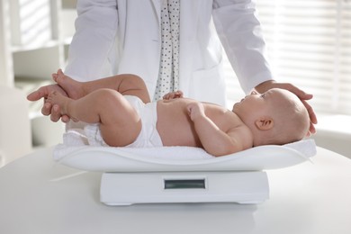 Pediatrician weighting little child in clinic, closeup. Checking baby's health