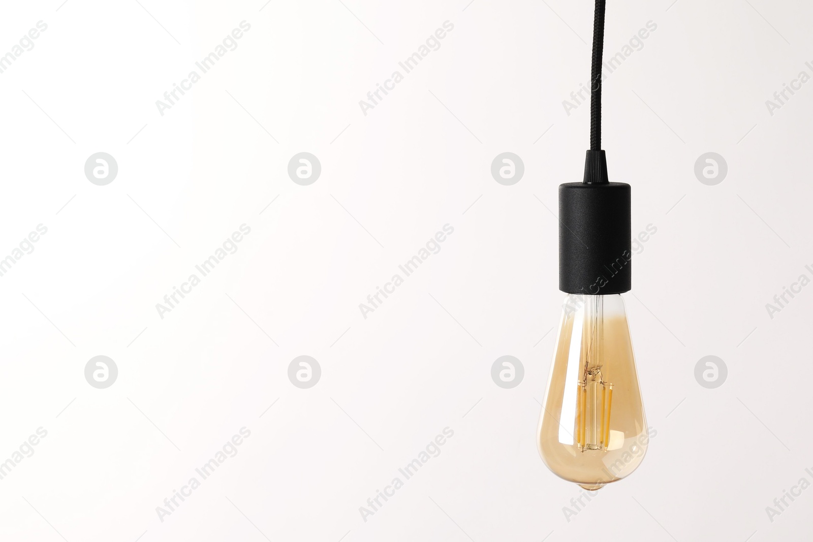 Photo of One light bulb hanging on cord against white background. Space for text