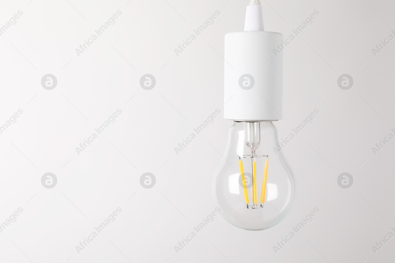 Photo of One light bulb hanging on cord against white background. Space for text