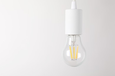 Photo of One light bulb hanging on cord against white background. Space for text