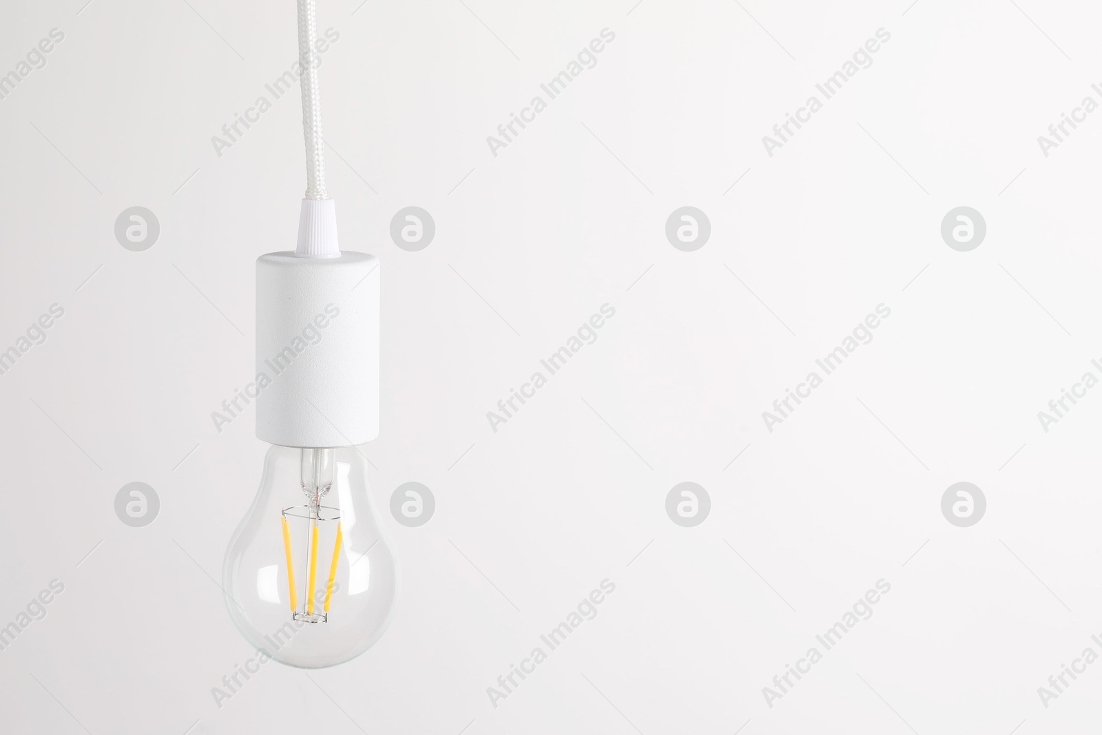 Photo of One light bulb hanging on cord against white background. Space for text