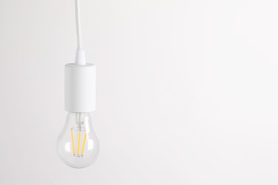 Photo of One light bulb hanging on cord against white background. Space for text