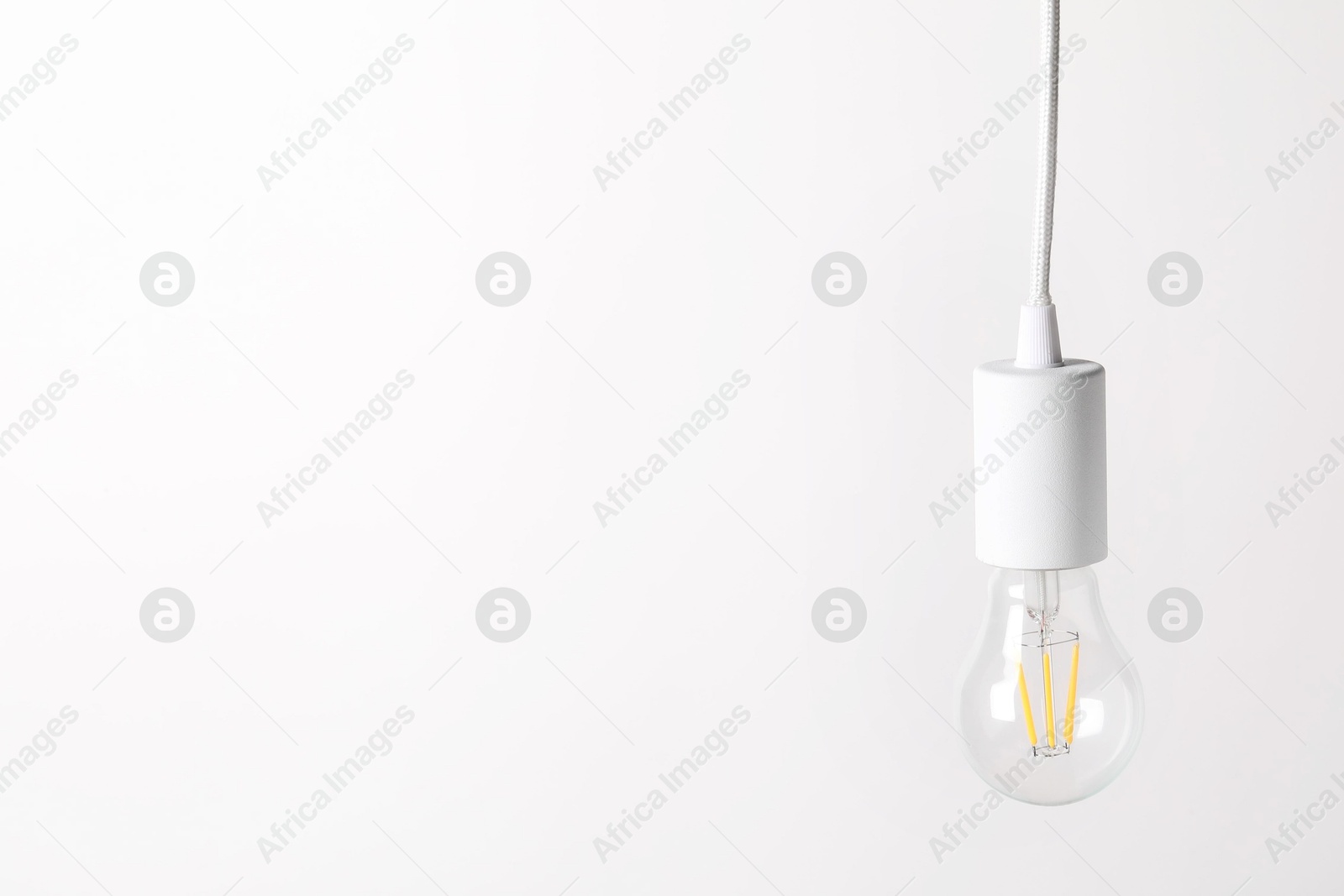 Photo of One light bulb hanging on cord against white background. Space for text