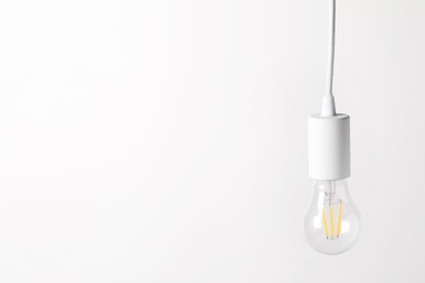 Photo of One light bulb hanging on cord against white background. Space for text