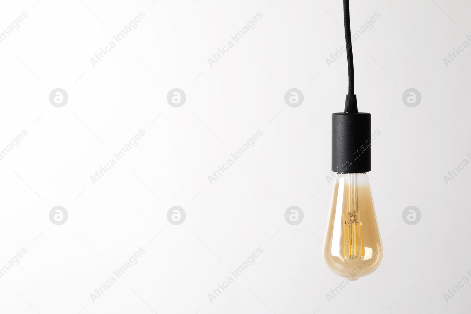 Photo of One light bulb hanging on cord against white background. Space for text