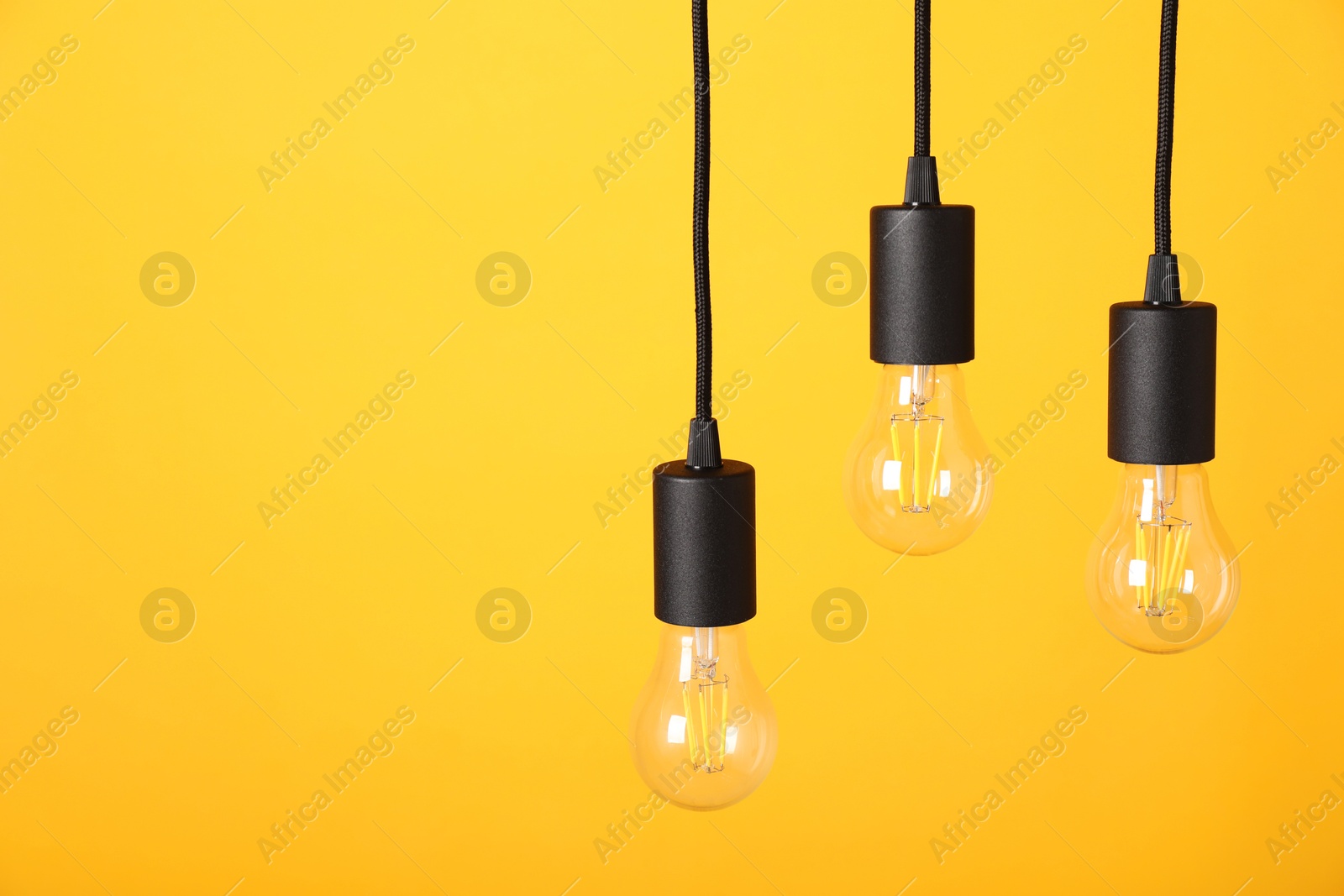 Photo of Light bulbs hanging on cords against orange background, space for text