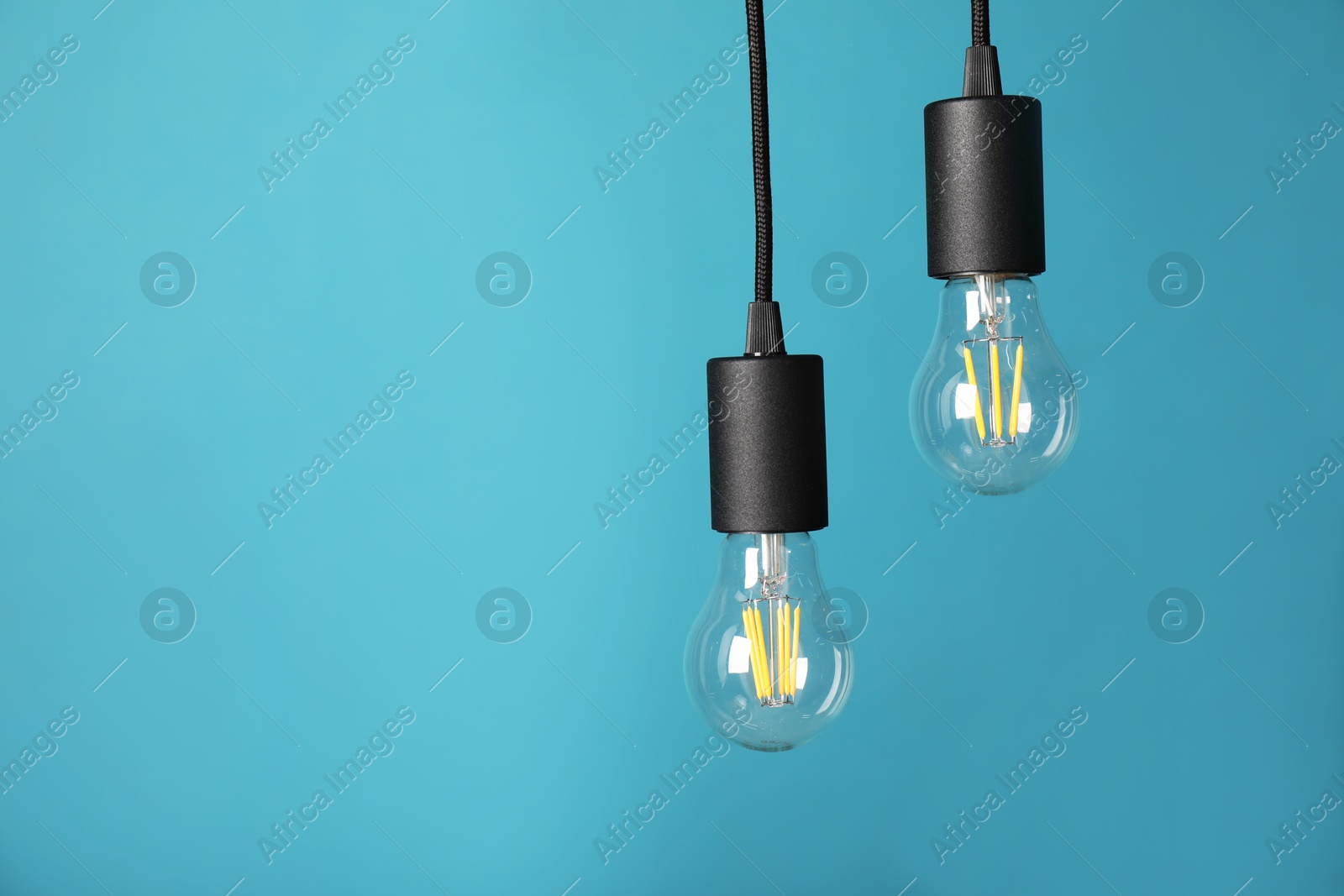 Photo of Light bulbs hanging on cords against light blue background, space for text