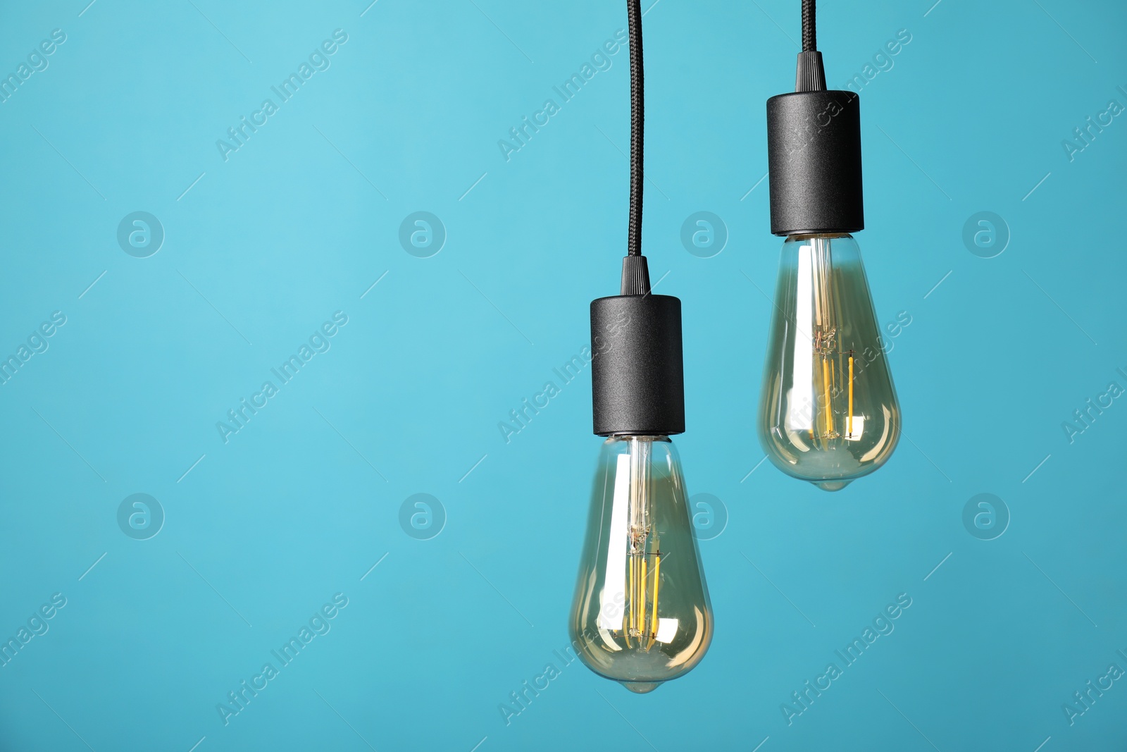 Photo of Light bulbs hanging on cords against light blue background, space for text