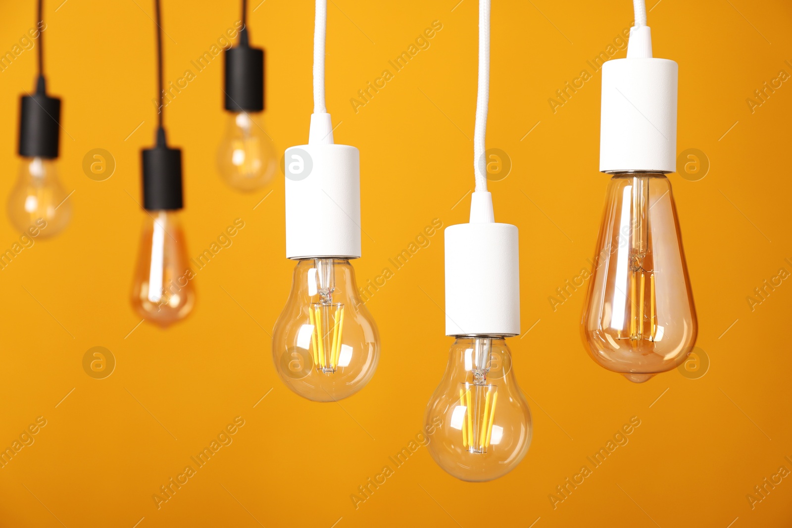 Photo of Light bulbs hanging on cords against orange background