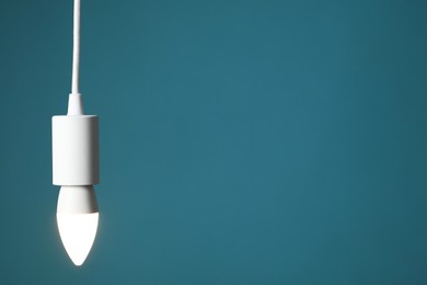 Photo of Light bulb hanging on cord against teal background, space for text