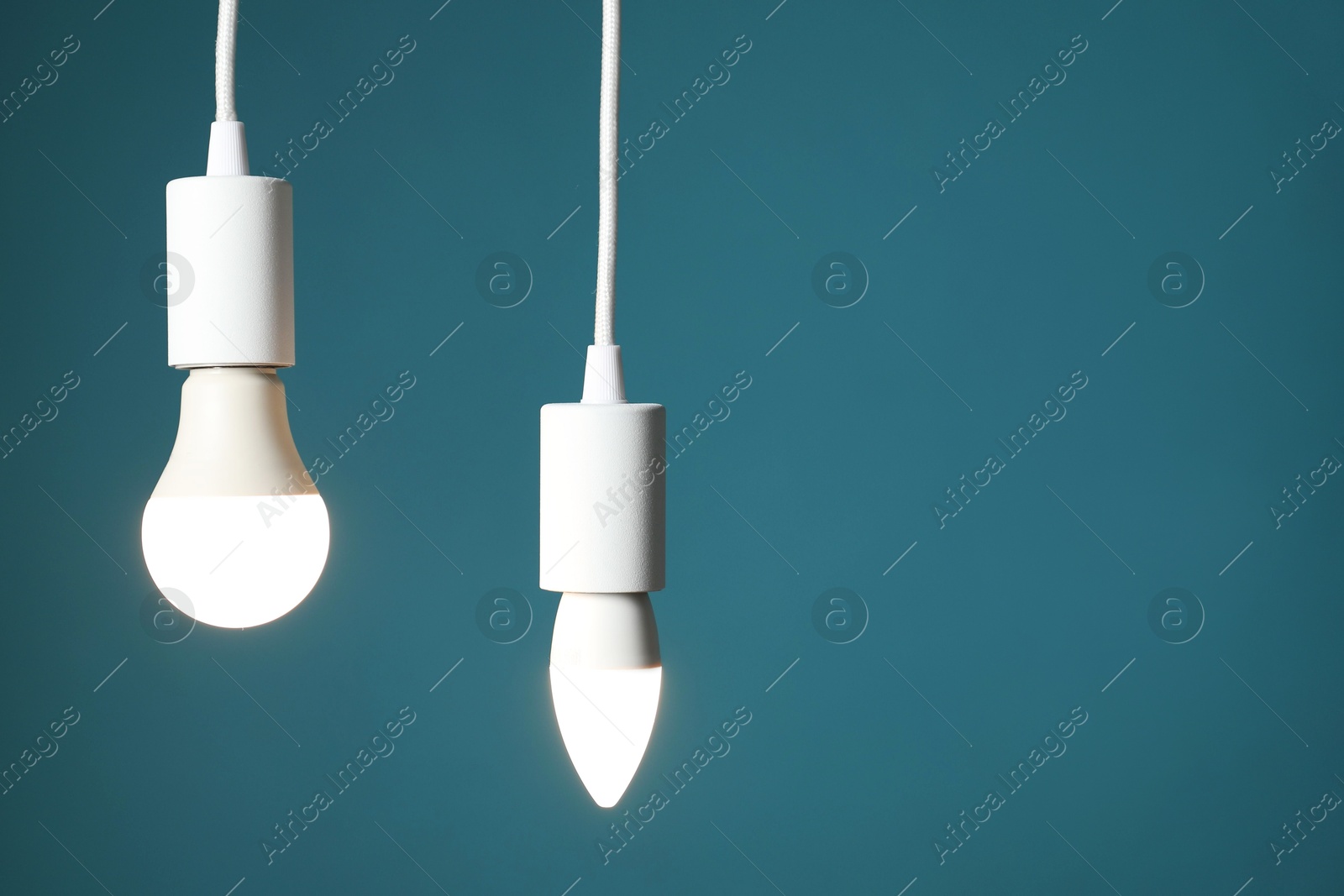 Photo of Light bulbs hanging on cords against teal background, space for text