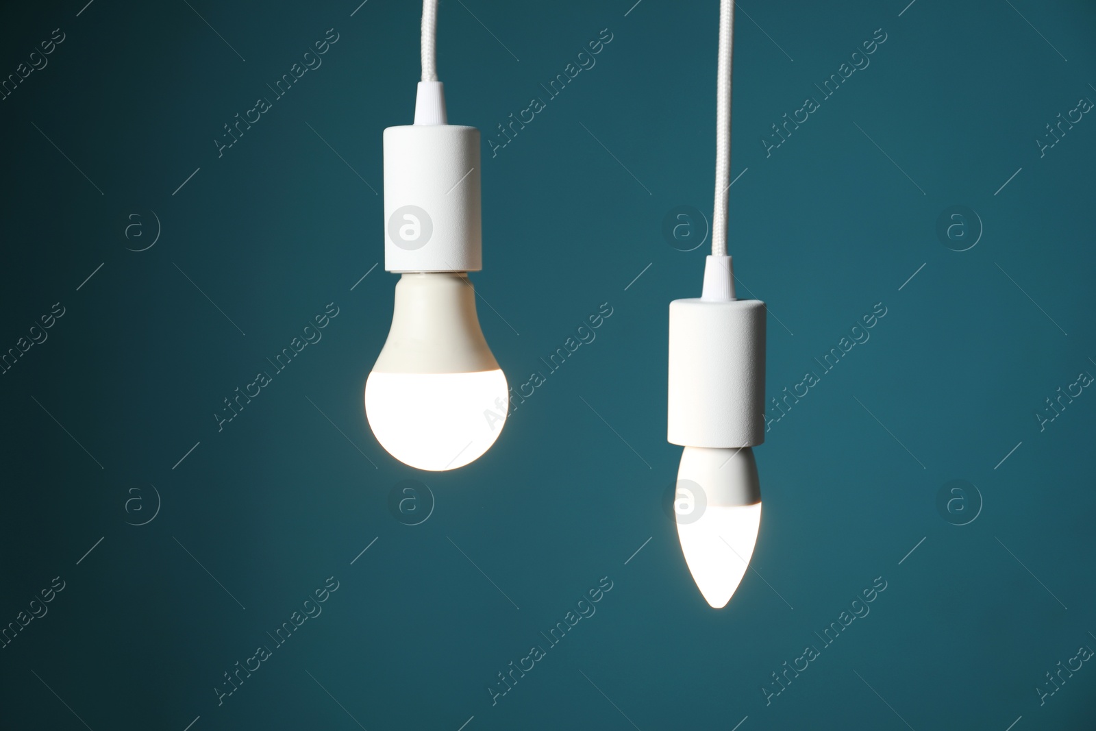 Photo of Light bulbs hanging on cords against teal background