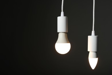 Photo of Light bulbs hanging on cords against grey background, space for text