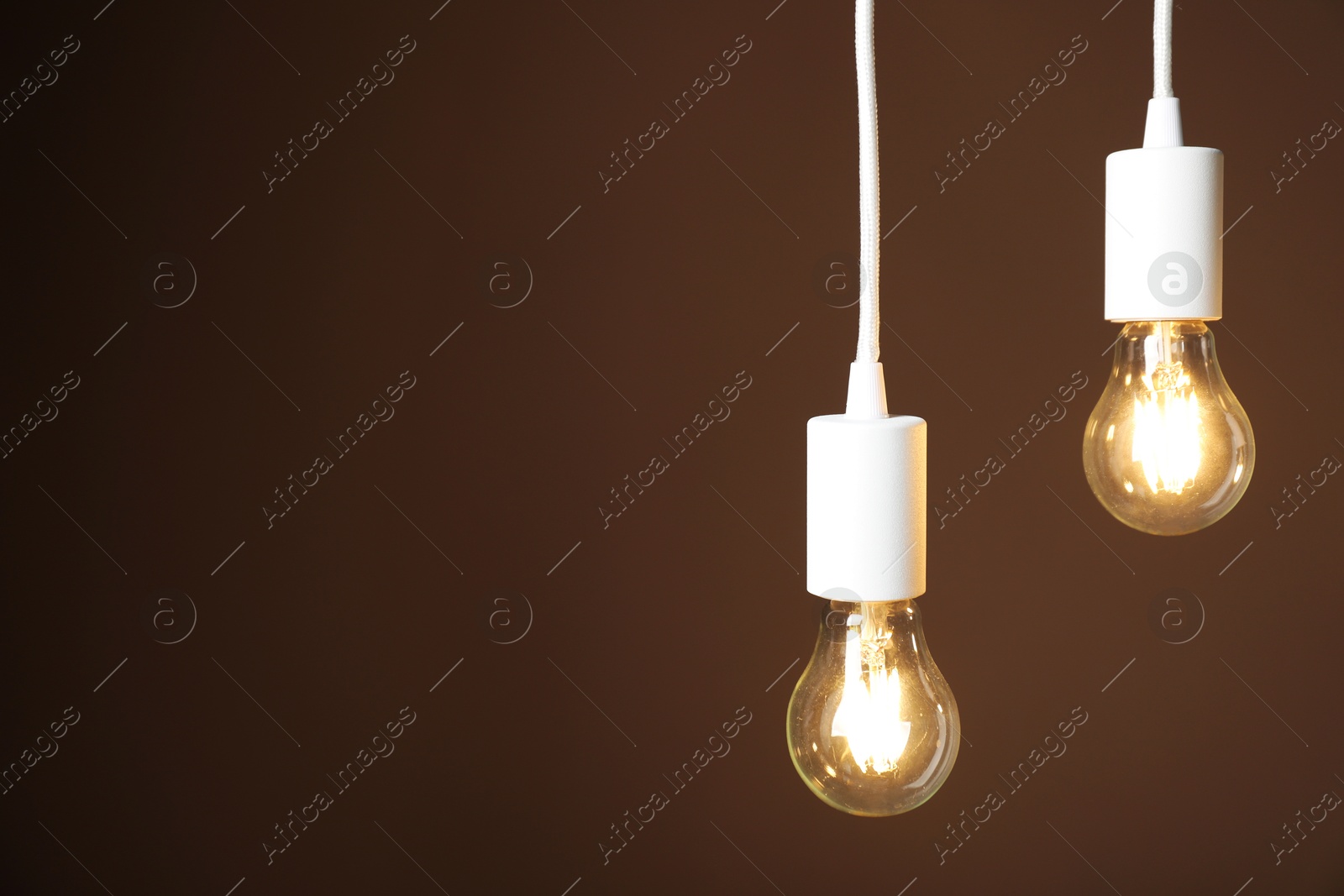 Photo of Light bulbs hanging on cords against brown background, space for text