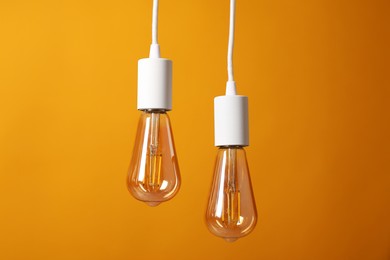 Photo of Light bulbs hanging on cords against orange background