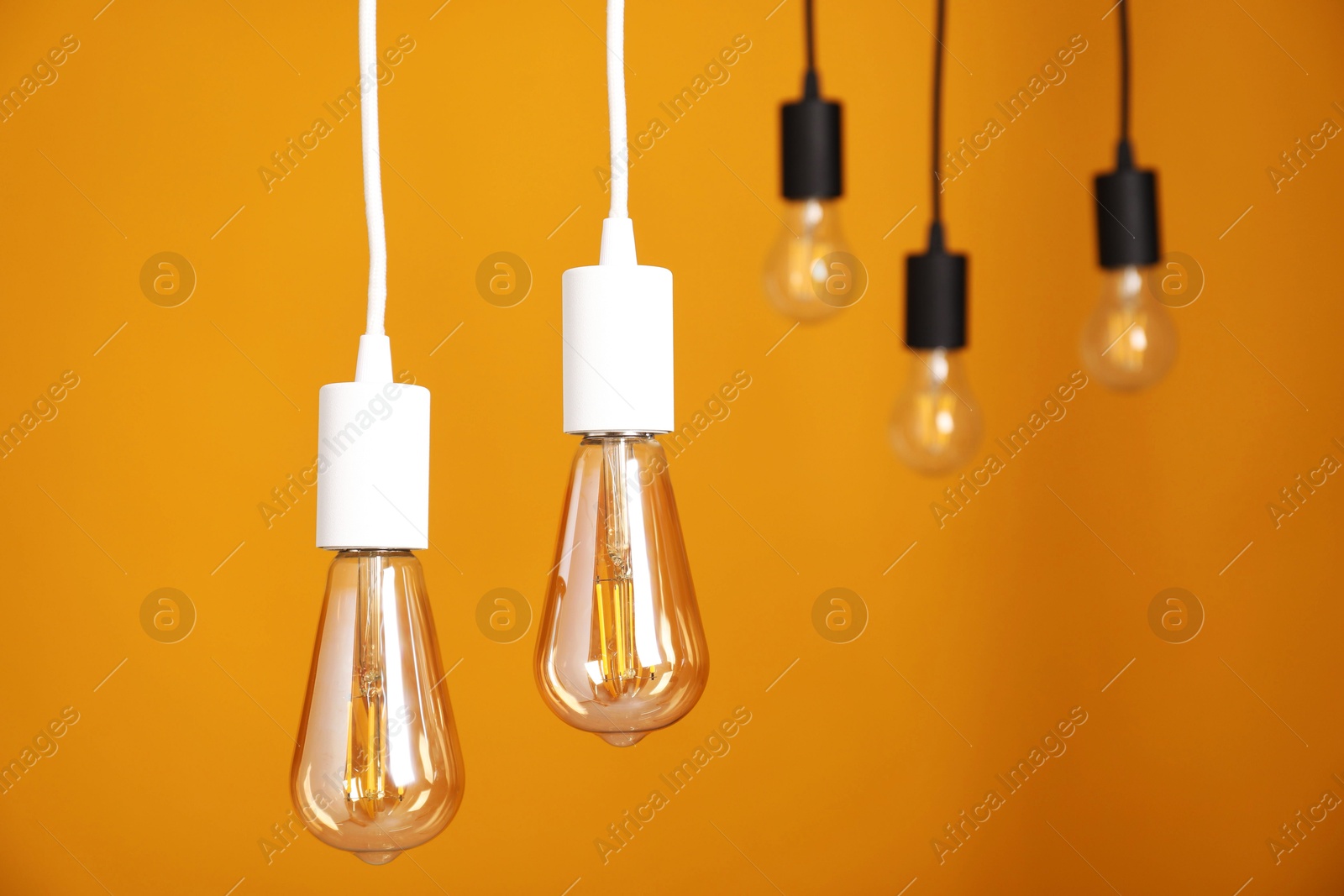 Photo of Light bulbs hanging on cords against orange background