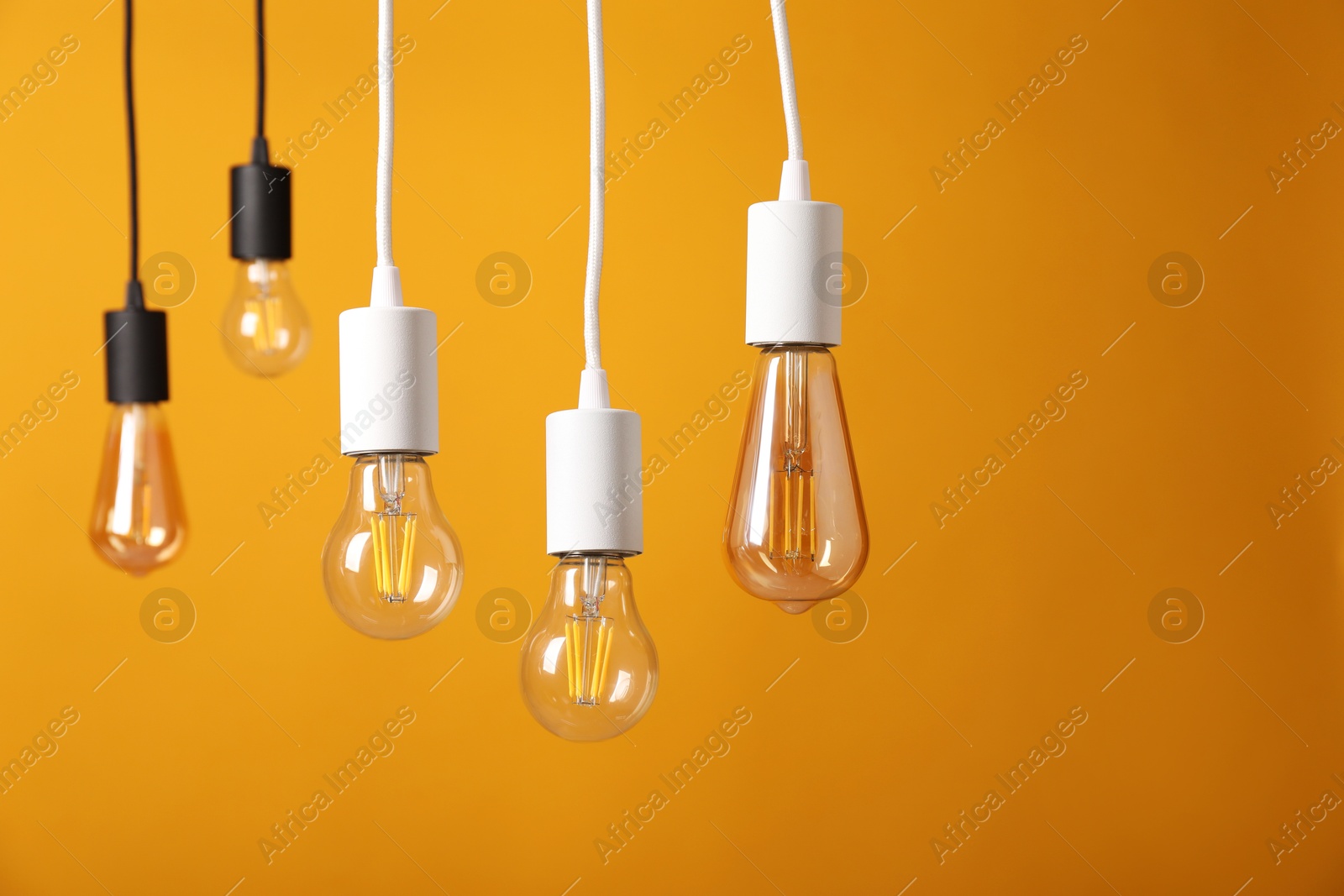 Photo of Light bulbs hanging on cords against orange background