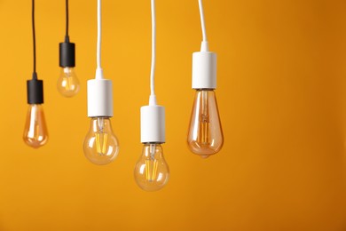 Photo of Light bulbs hanging on cords against orange background