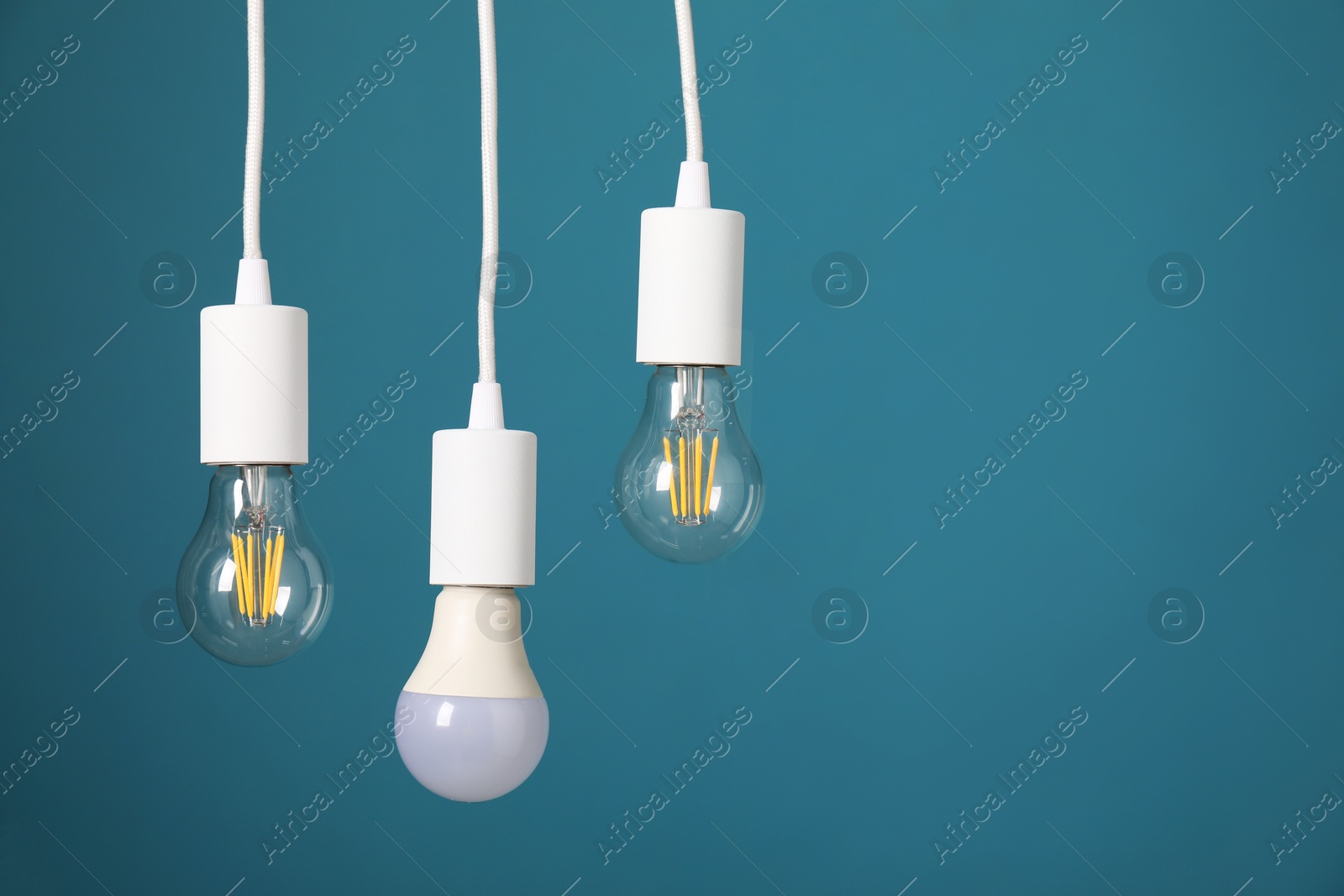 Photo of Light bulbs hanging on cords against light blue background, space for text