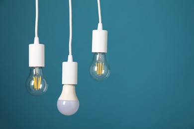 Photo of Light bulbs hanging on cords against light blue background, space for text