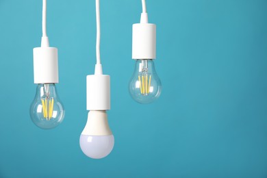 Photo of Light bulbs hanging on cords against light blue background, space for text