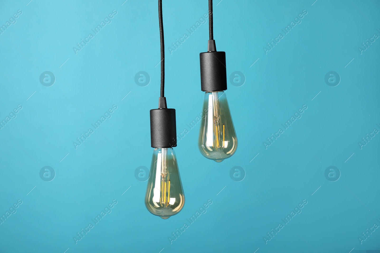 Photo of Light bulbs hanging on cords against light blue background