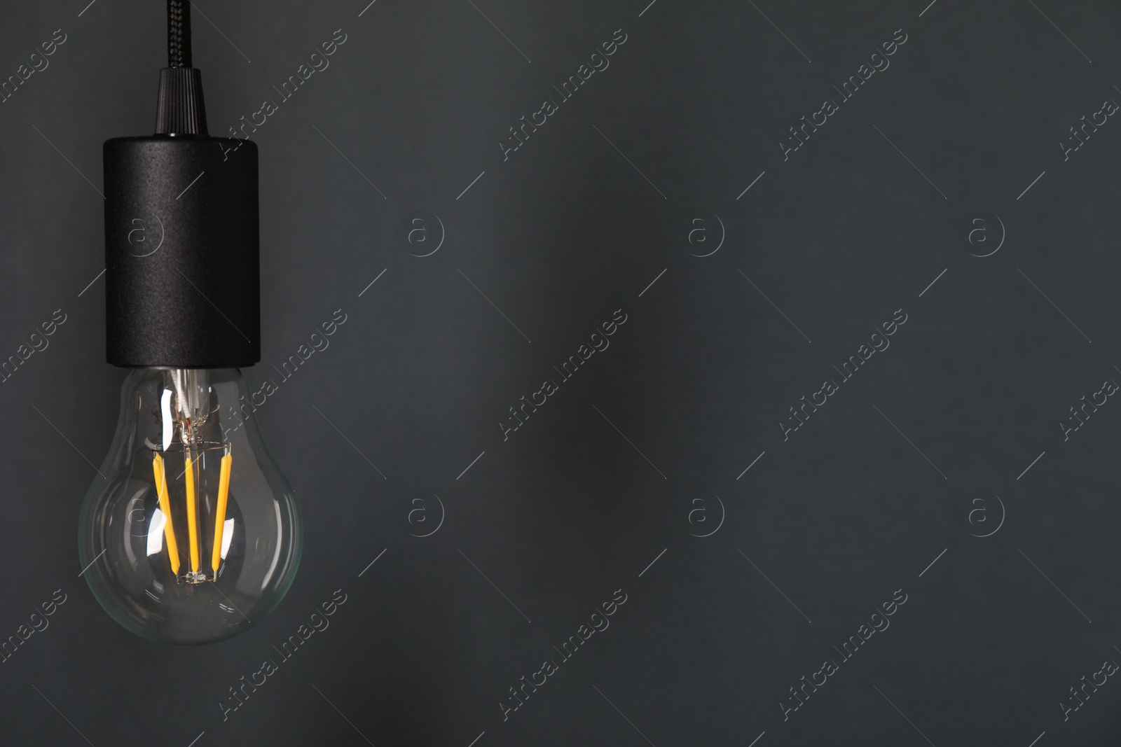 Photo of One light bulb hanging on cord against grey background, space for text