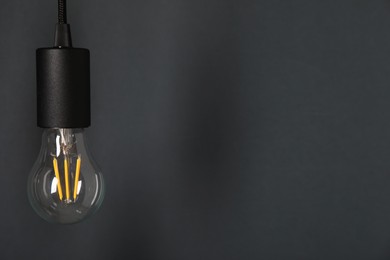 Photo of One light bulb hanging on cord against grey background, space for text