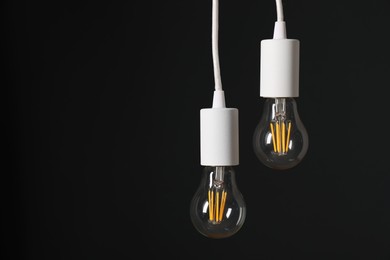 Photo of Light bulbs hanging on cords against black background, space for text