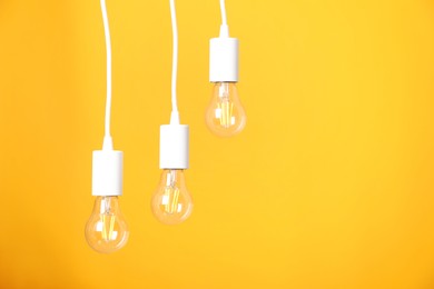 Photo of Light bulbs hanging on cords against orange background, space for text