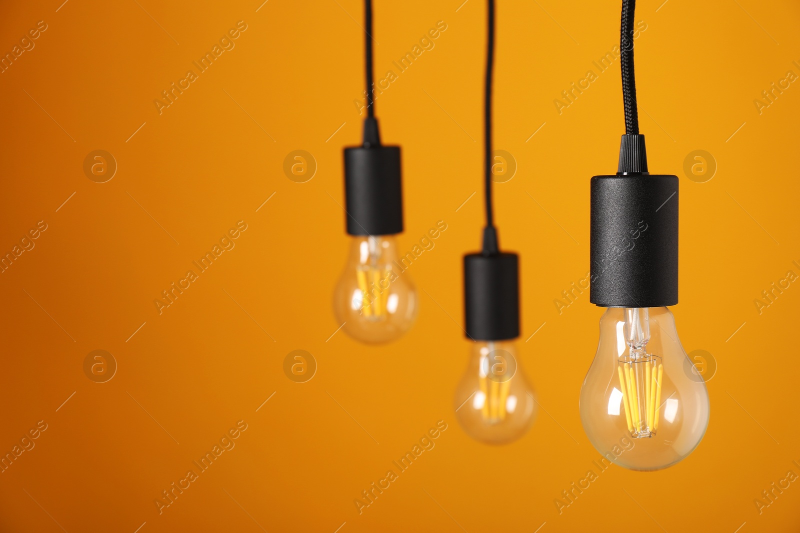 Photo of Light bulbs hanging on cords against orange background, space for text