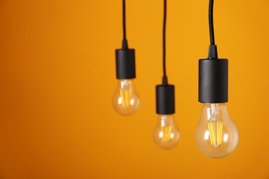 Photo of Light bulbs hanging on cords against orange background, space for text