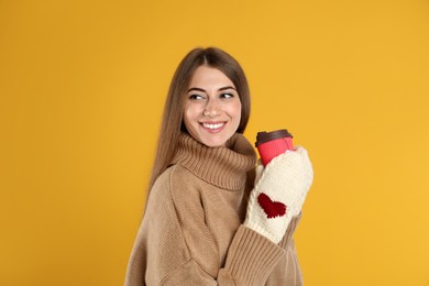 Photo of Happy beautiful woman with paper cup of mulled wine on yellow background