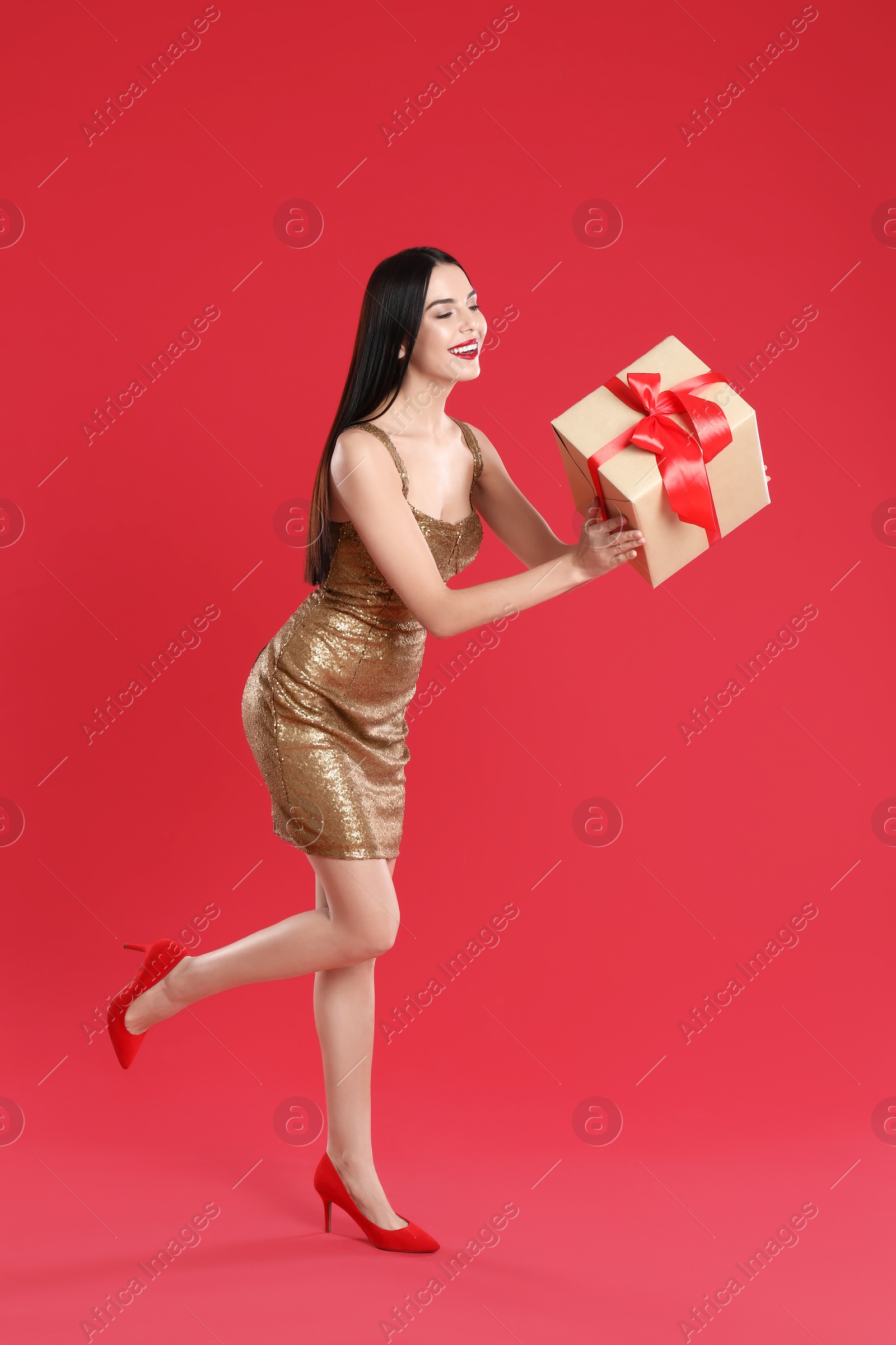 Photo of Woman in golden dress holding Christmas gift on red background