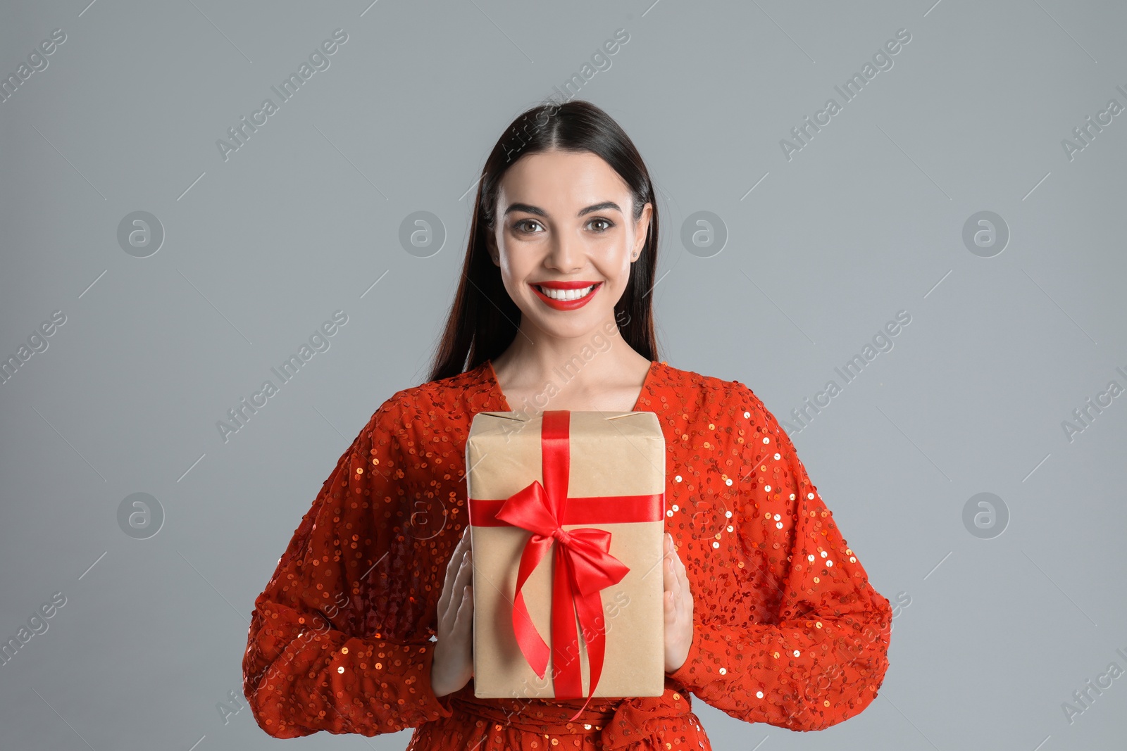 Photo of Woman in red dress holding Christmas gift on grey background