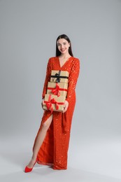 Photo of Woman in red dress holding Christmas gifts on grey background