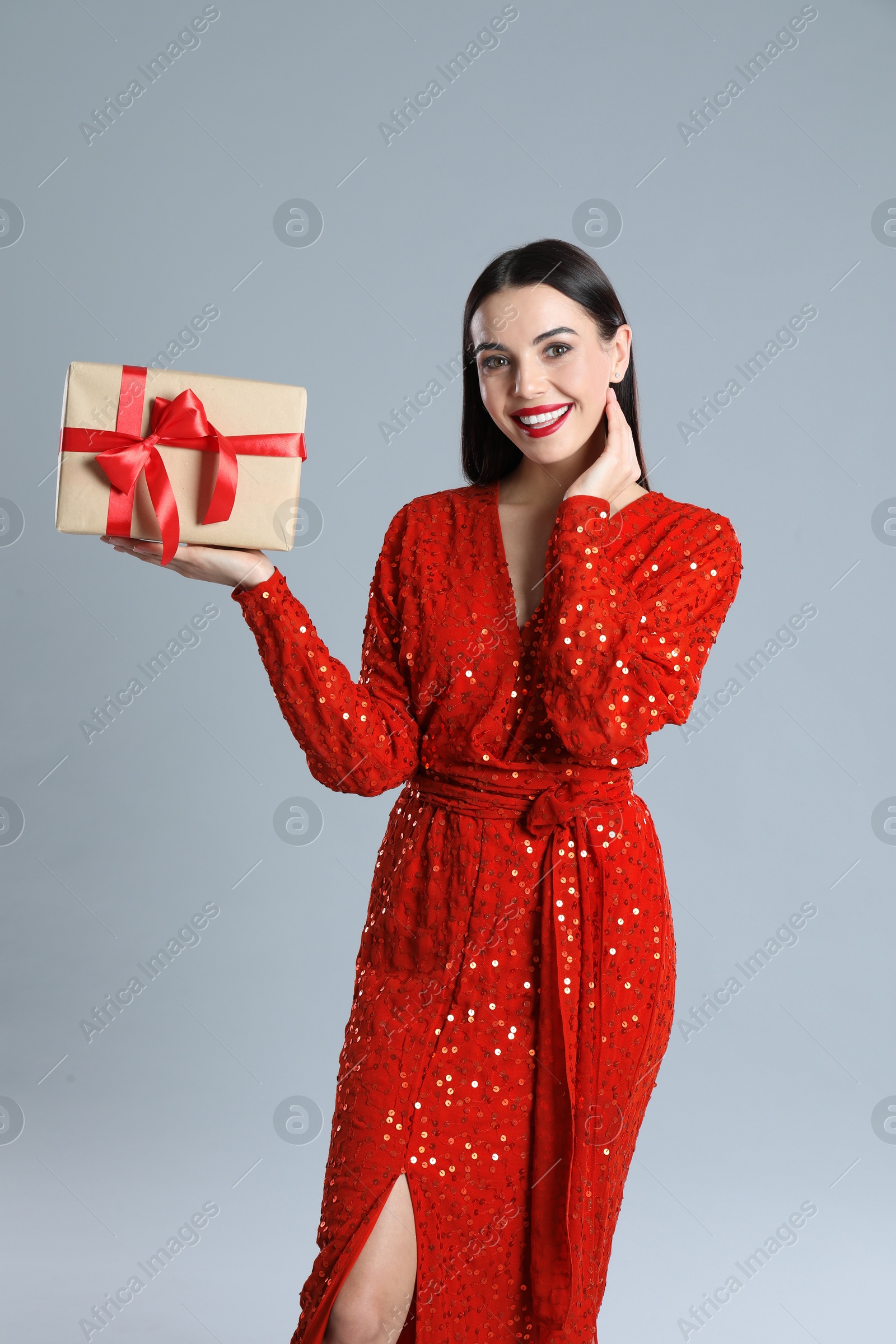 Photo of Woman in red dress holding Christmas gift on grey background