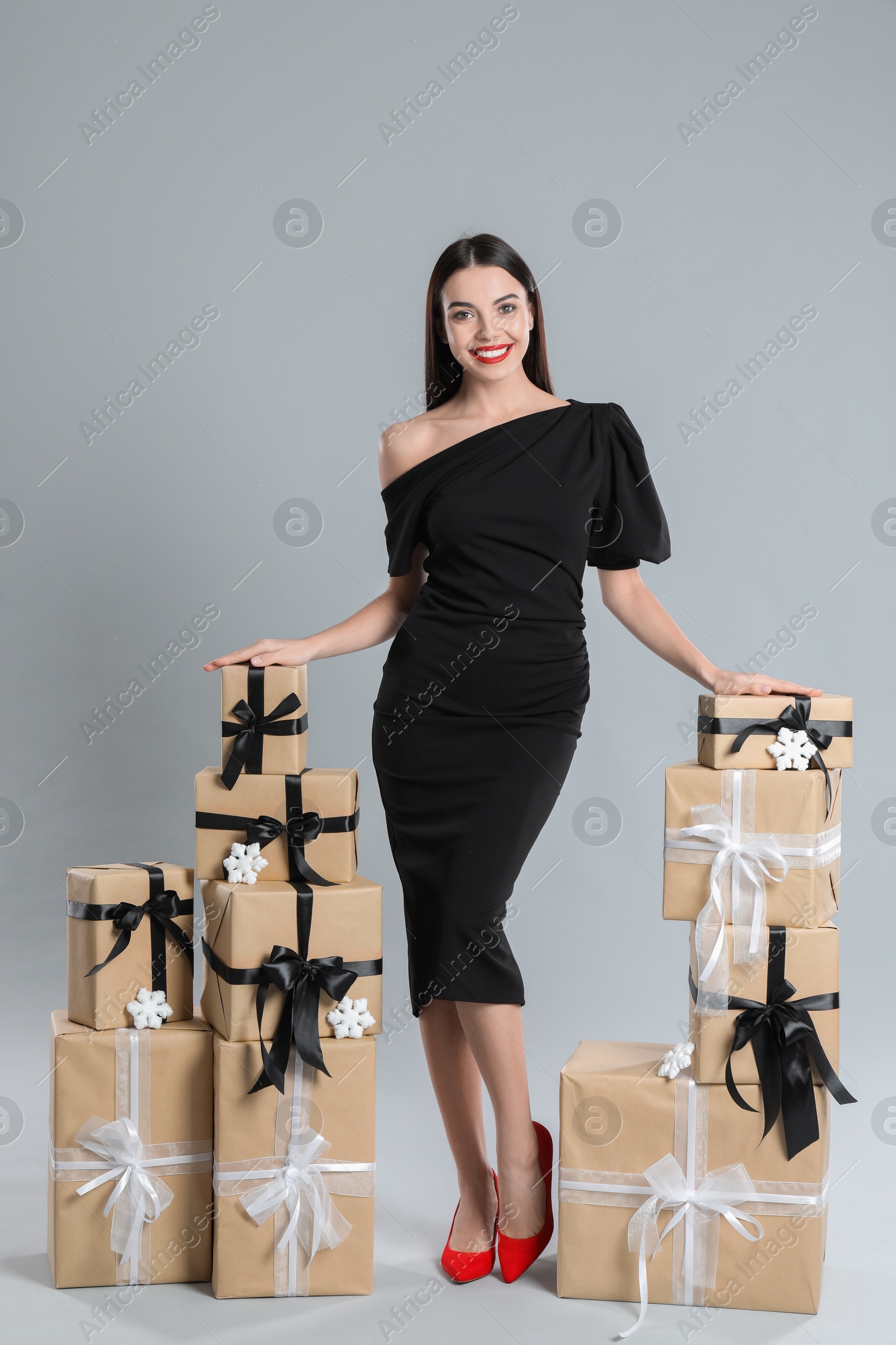 Photo of Woman in black dress with Christmas gifts on grey background