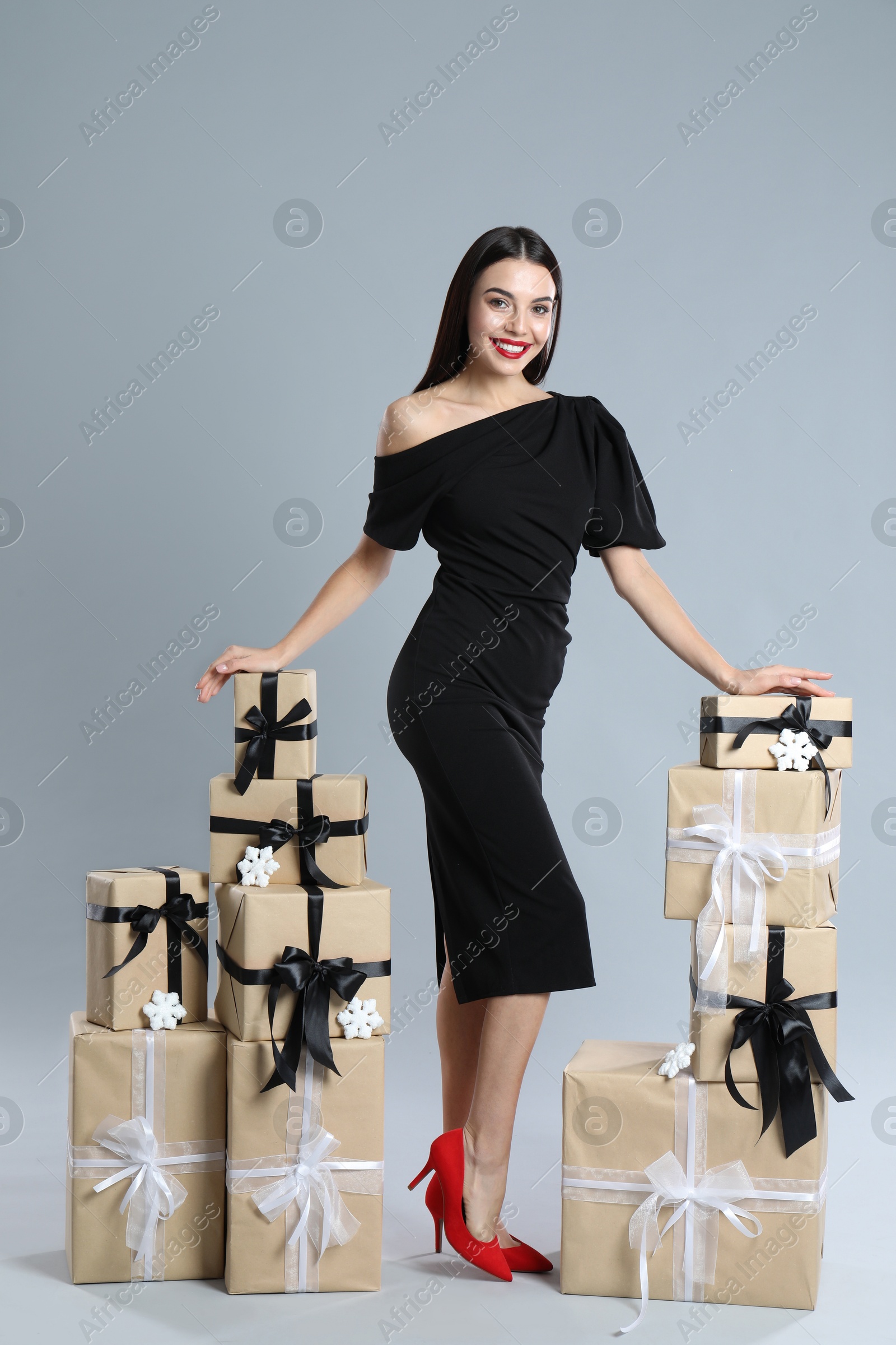 Photo of Woman in black dress with Christmas gifts on grey background