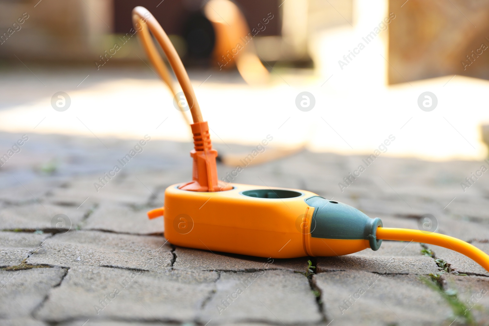 Photo of Orange extension cord outdoors on sunny day, closeup