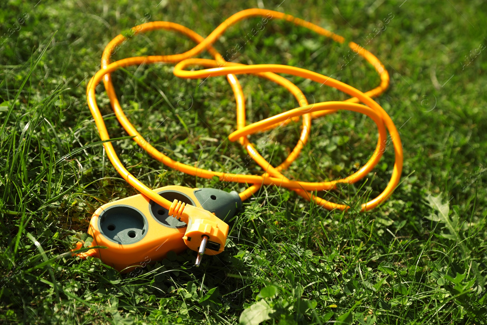 Photo of Orange extension cord on green grass outdoors, closeup