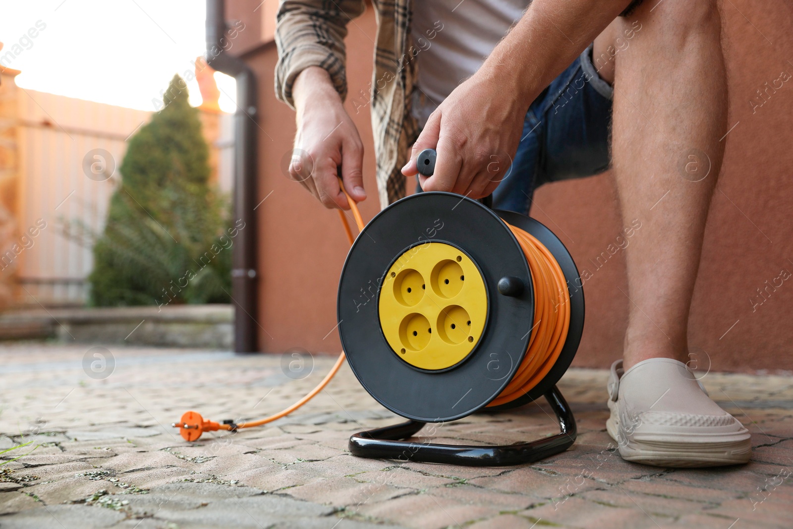 Photo of Man with extension cord reel in backyard, closeup. Space for text